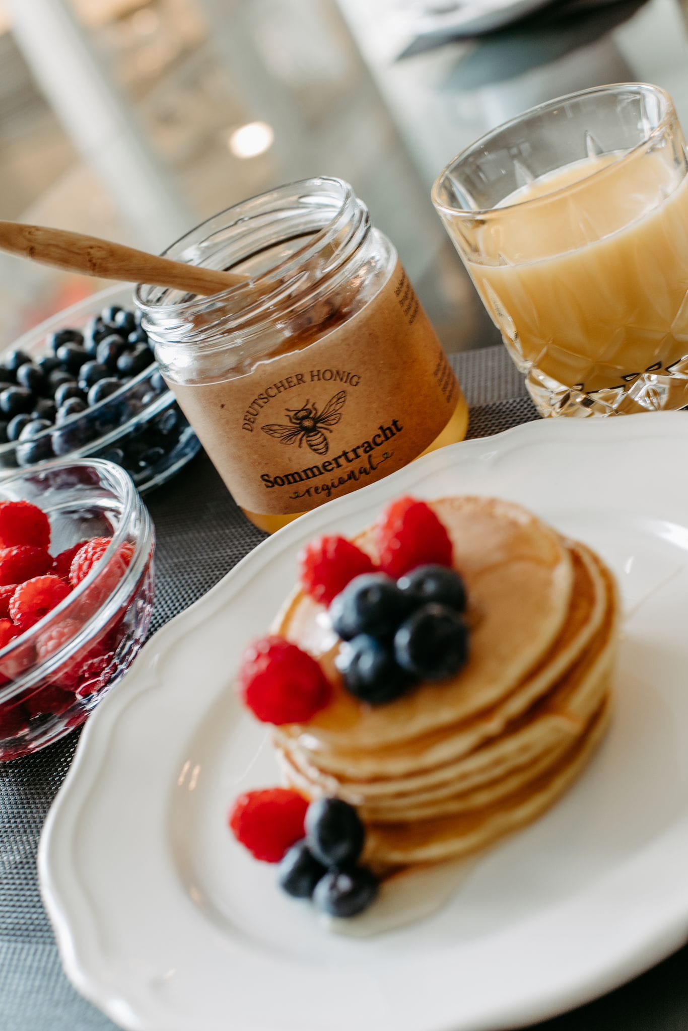 Sommertracht Honig mit Pancakes, Himbeeren und Heidelbeeren zum Frühstück